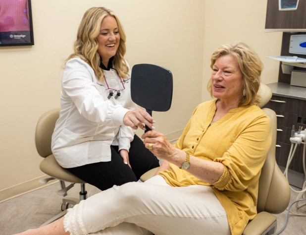 Two women examine a dental model in a bright clinical office setting.