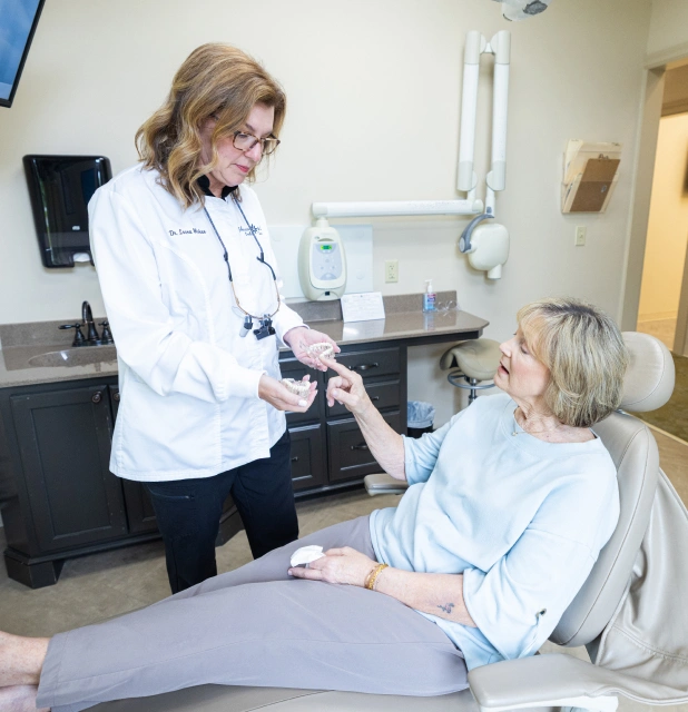 Female dentist in white coat examining patient in dental chair at clinical office.