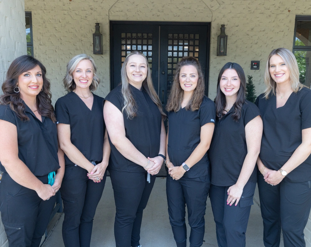 Six dental care professionals in black uniforms standing together in front of a dark wooden door.