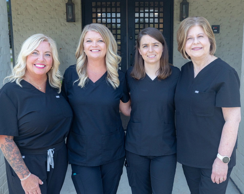 Four dental care professionals in black scrubs standing together outside a brick building entrance.