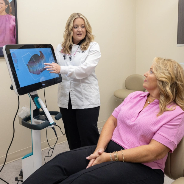 Dental professional showing patient digital scan results on tablet screen in clinical office setting.