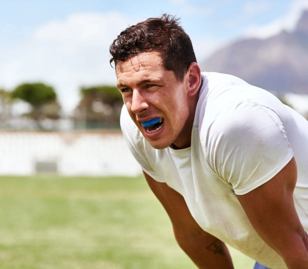 Man wearing blue mouthguard in athletic stance outdoors on grass field.