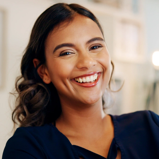 Smiling woman in dark blue scrubs in dental office setting, representing dental care professional.