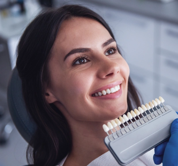 Smiling woman holding dental shade guide in modern dental office setting.
