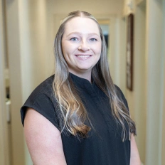 Smiling woman with long hair in black shirt in dental office hallway.