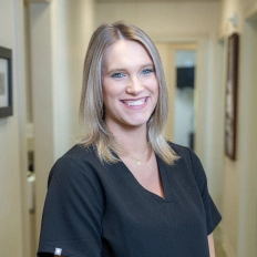 Professional dental care staff member smiling in clinical hallway setting.
