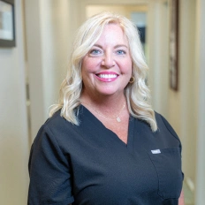 Professional dental staff member smiling in clinical office setting wearing scrubs