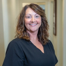 Woman in black scrubs smiling at camera in dental office hallway setting