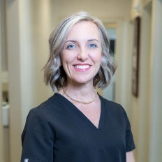 Professional portrait of smiling woman in black scrubs at dental office